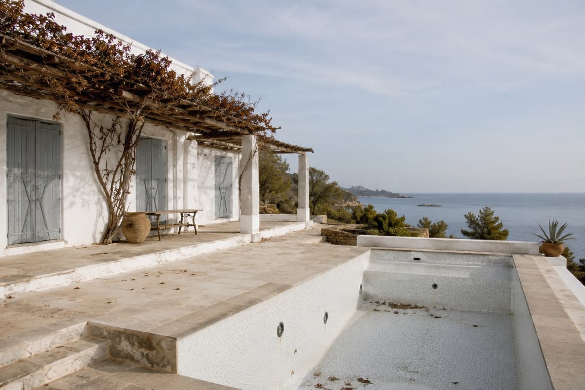 An empty villa pool and pergola in winter, sea in the background under flat light