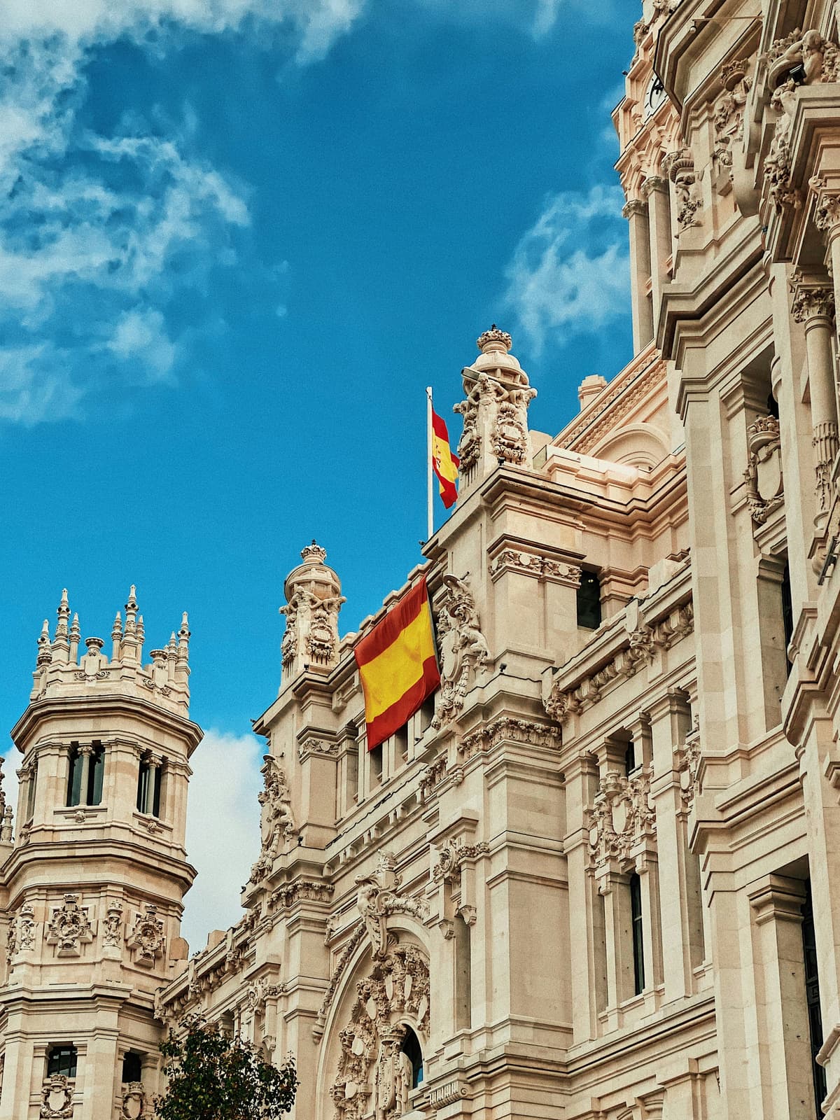 The Spanish flag flying from the ornate stone facade of a grand government building in Madrid against a blue sky